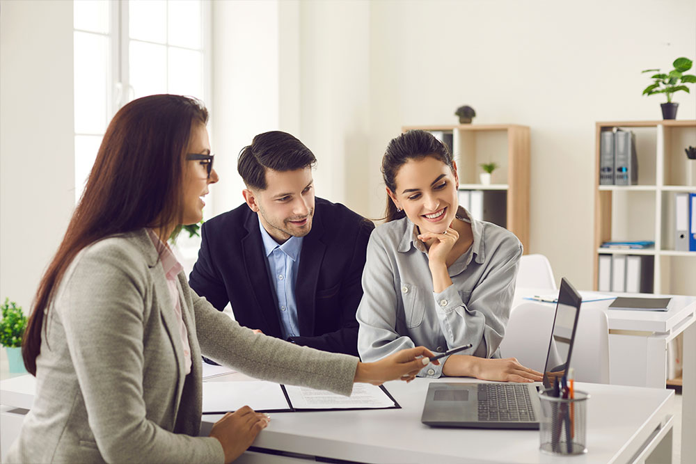 A group of three coworkers in a bright office sharing a moment of collaboration at a desk with laptops - https://www.quincymutual.com/index.htm
