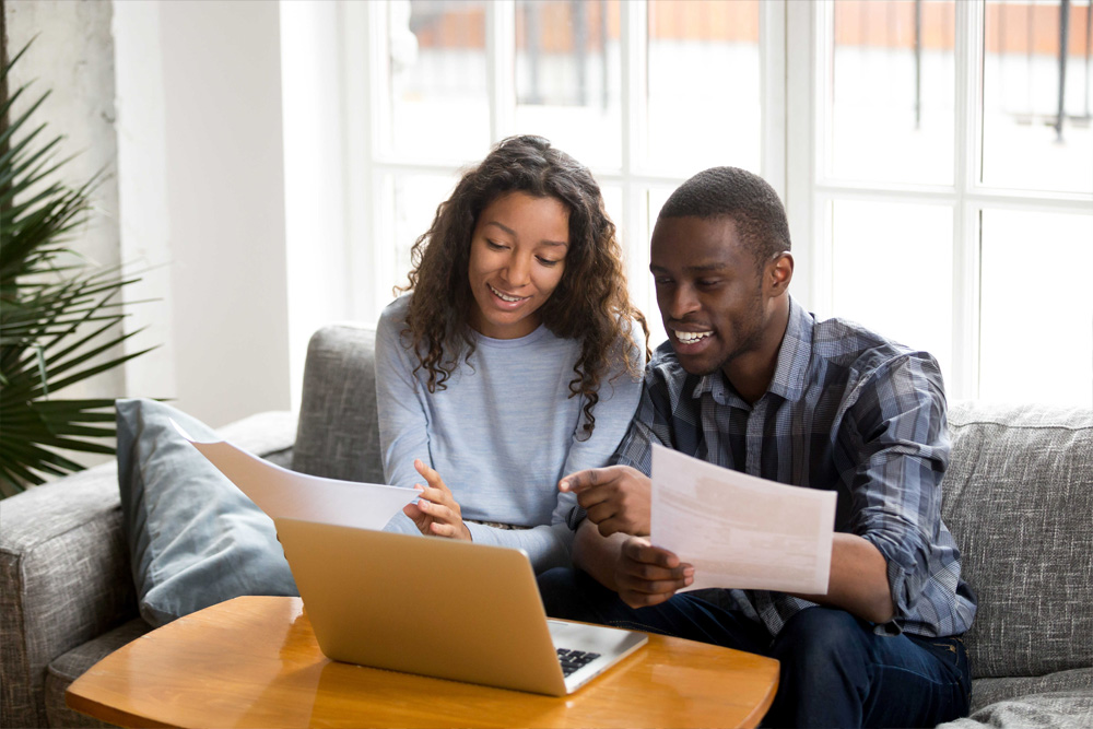 Two people sitting on a couch at home, reviewing printed documents on a laptop together - https://www.quincymutual.com/index.htm