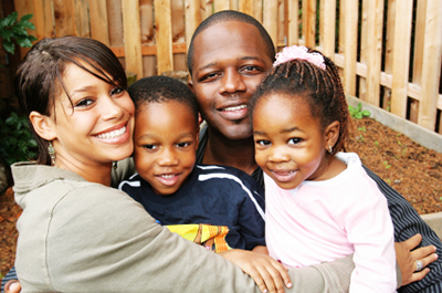 An African American family standing in the corner of their fenced in yard smiling at the camera. = https://www.quincymutual.com/index.htm