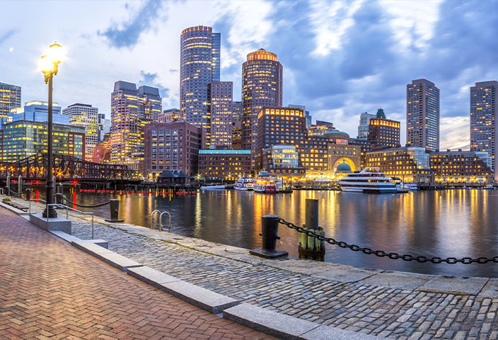 Panoramic view of the Boston skyline and Harbor at twilight, featuring the illuminated Rowes Wharf. - www.quincymutual.com