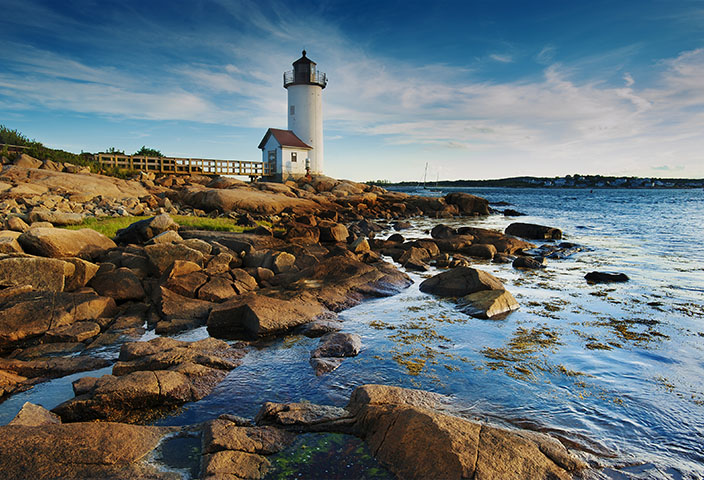 Annisquam Harbor Lighthouse with a wooden walkway on a rocky shoreline in Gloucester, Massachusetts. - www.quincymutual.com