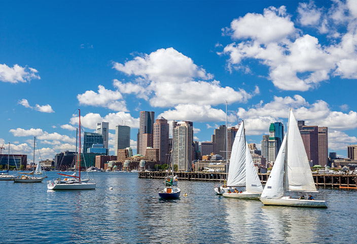 Boston Harbor skyline view with sailboats on blue water under a cloudy sky. - www.quincymutual.com