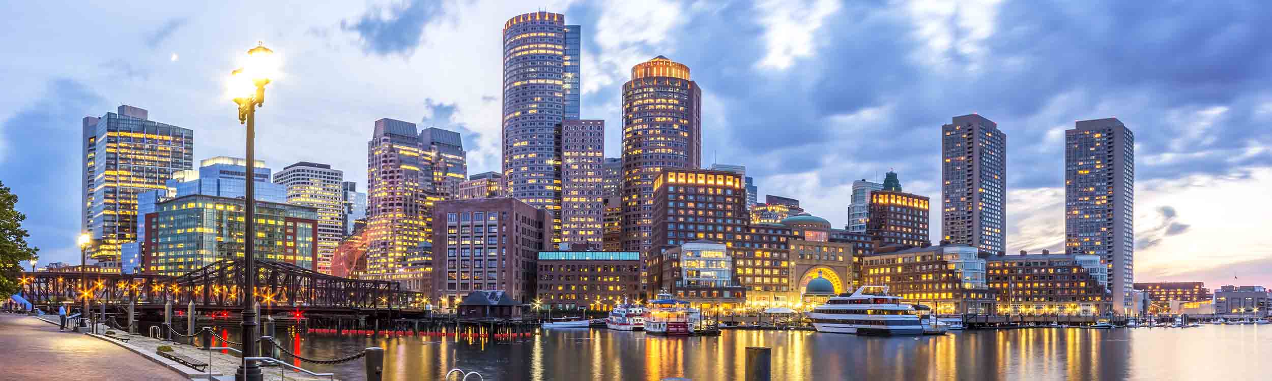 Panoramic view of the Boston skyline and Harbor at twilight, featuring the illuminated Rowes Wharf. - www.quincymutual.com