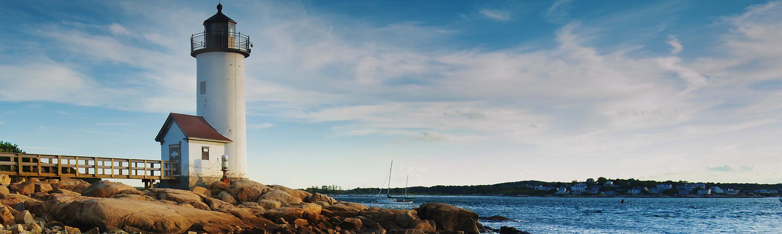 Annisquam Harbor Lighthouse with a wooden walkway on a rocky shoreline in Gloucester, Massachusetts. - www.quincymutual.com