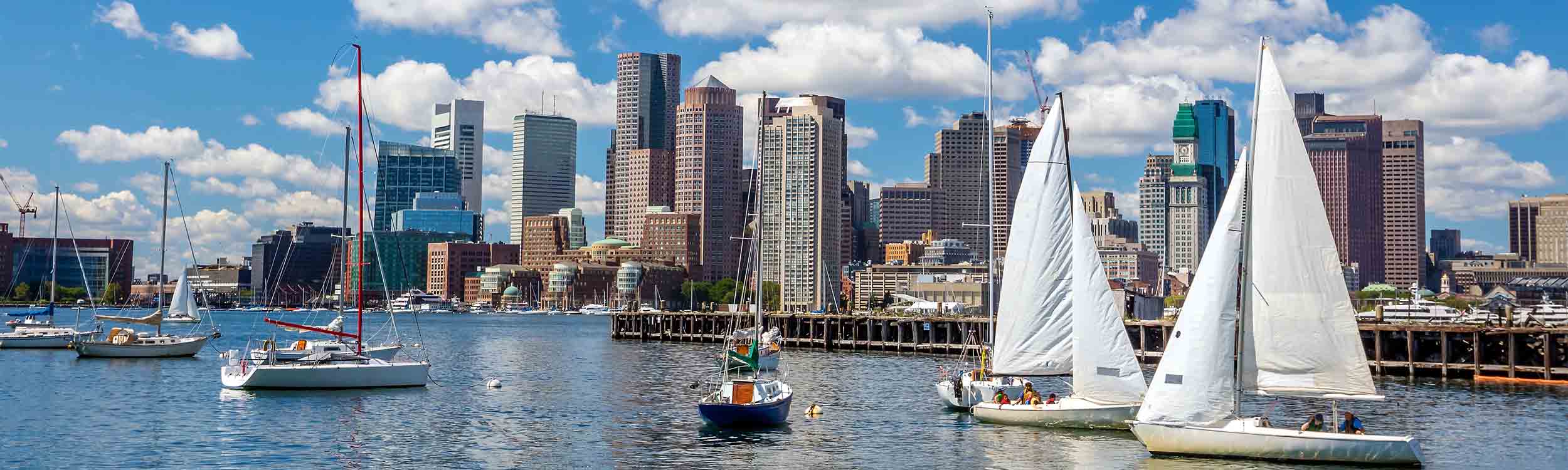 Boston Harbor skyline view with sailboats on blue water under a cloudy sky. - www.quincymutual.com