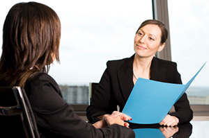 Two women meeting at a conference room table to discuss documents in a blue folder. = https://www.quincymutual.com/index.htm