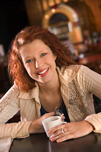 Woman seated at cafe table with cup of coffee in her hand smiling at camera. = https://www.quincymutual.com/index.htm